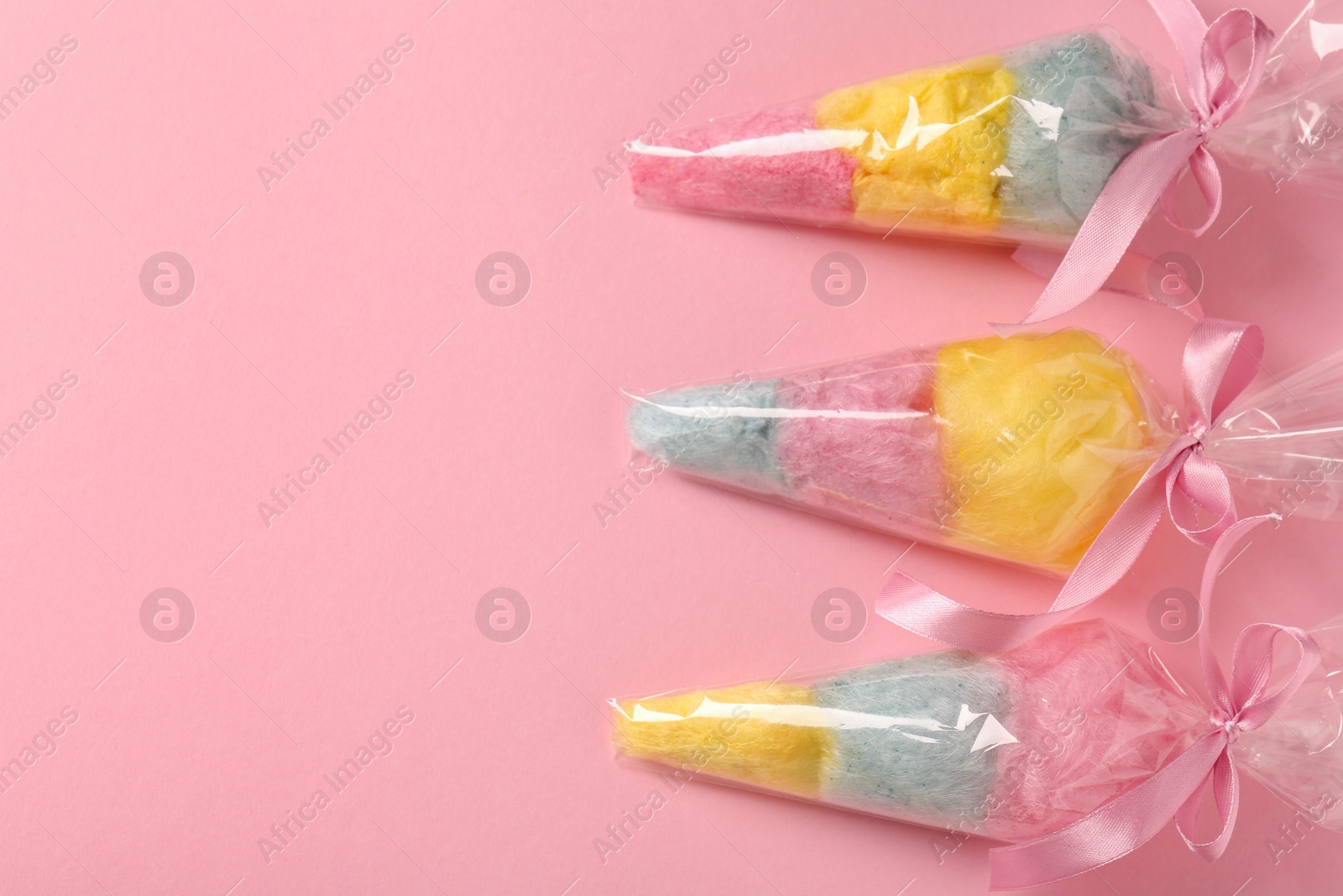 Photo of Packaged sweet cotton candies on pink background, flat lay. Space for text