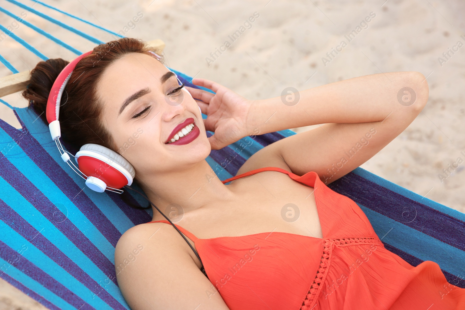 Photo of Young woman listening to music in comfortable hammock at seaside