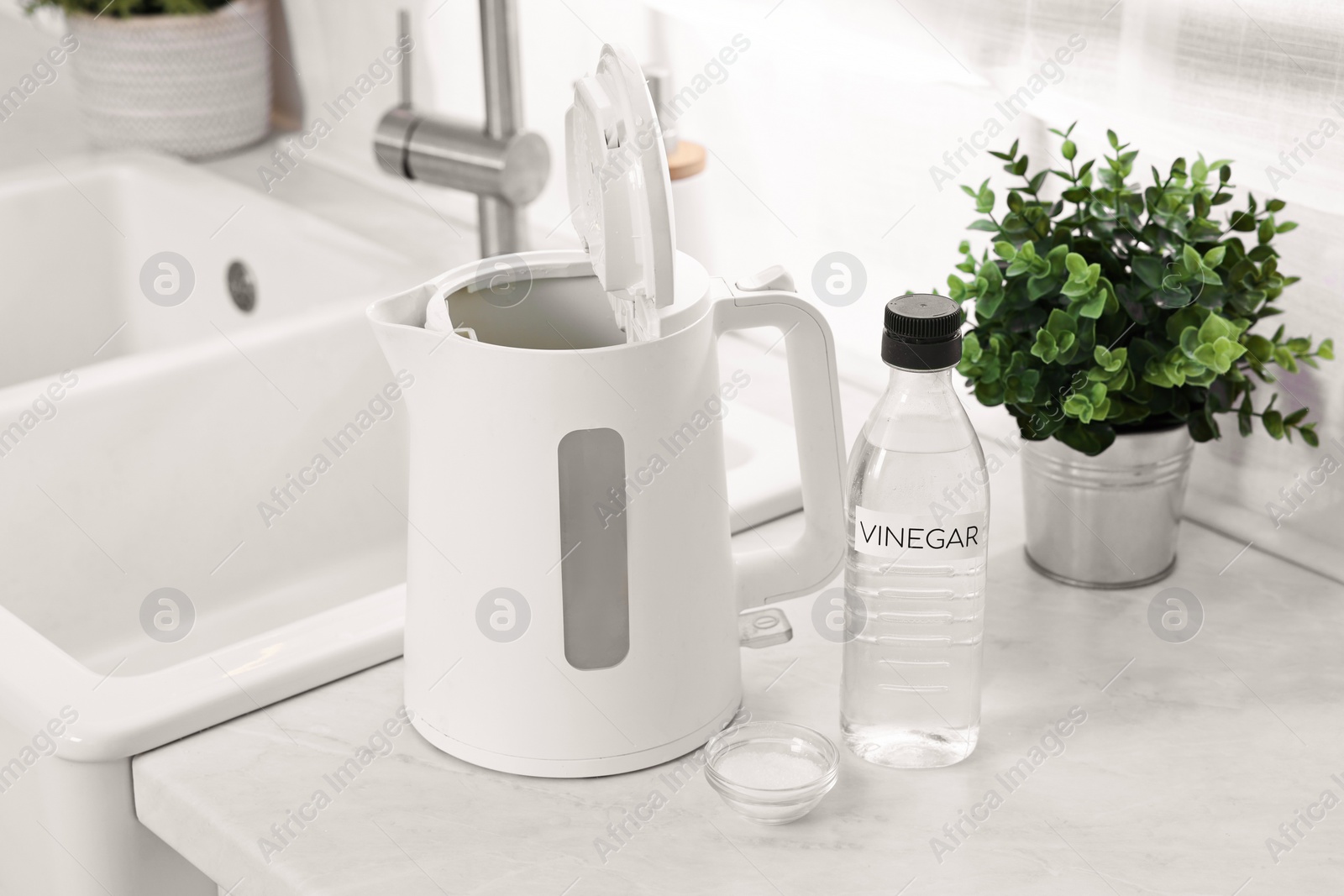 Photo of Cleaning electric kettle. Bottle of vinegar and baking soda on countertop in kitchen