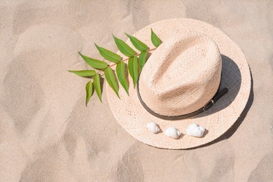 Photo of Straw hat, seashells and green leaves on sandy beach, top view. Space for text