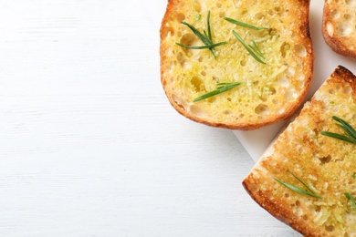 Slices of toasted bread with garlic and herb on white wooden table, top view. Space for text