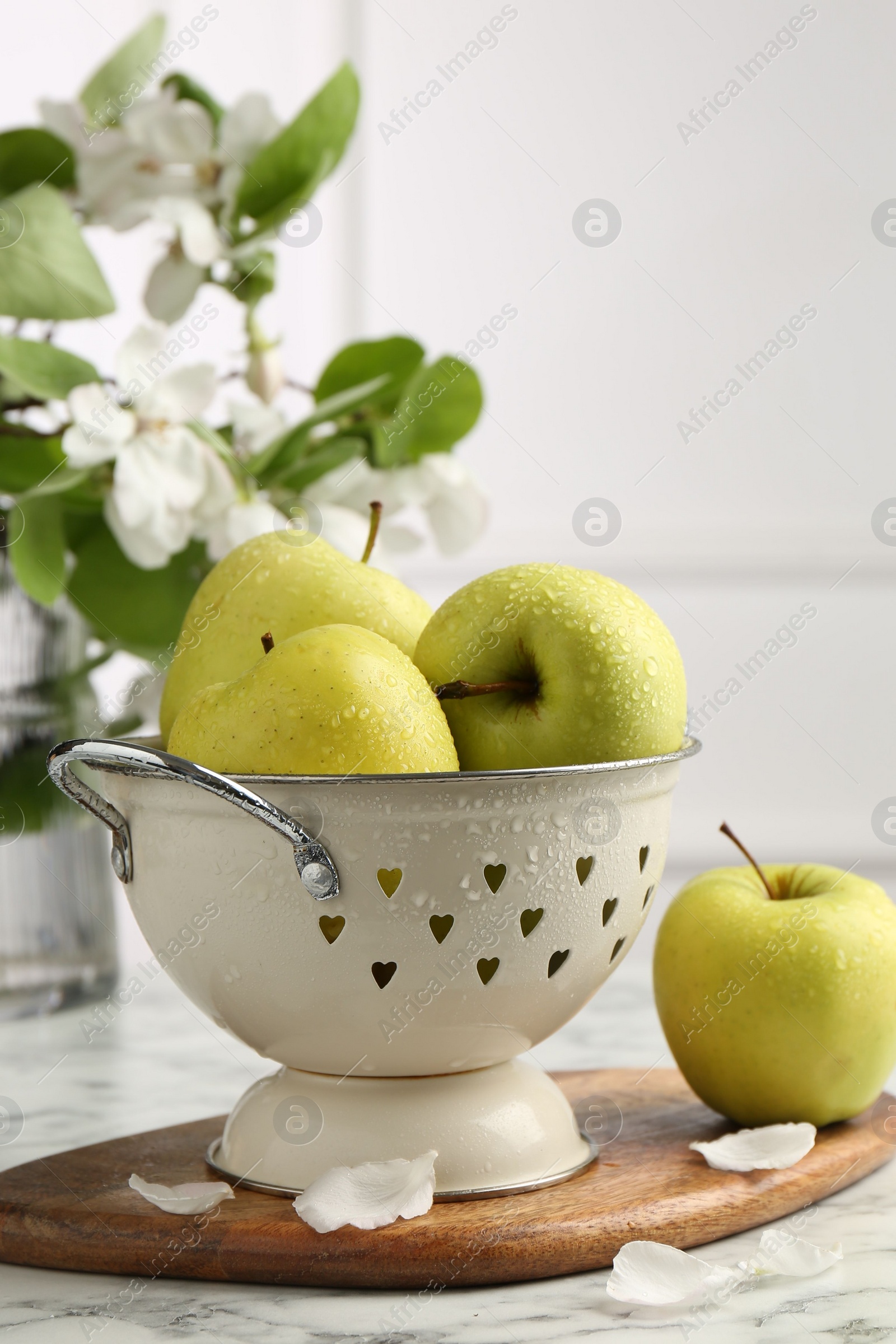 Photo of Colander with fresh apples and flower petals on white marble table