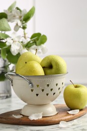 Colander with fresh apples and flower petals on white marble table