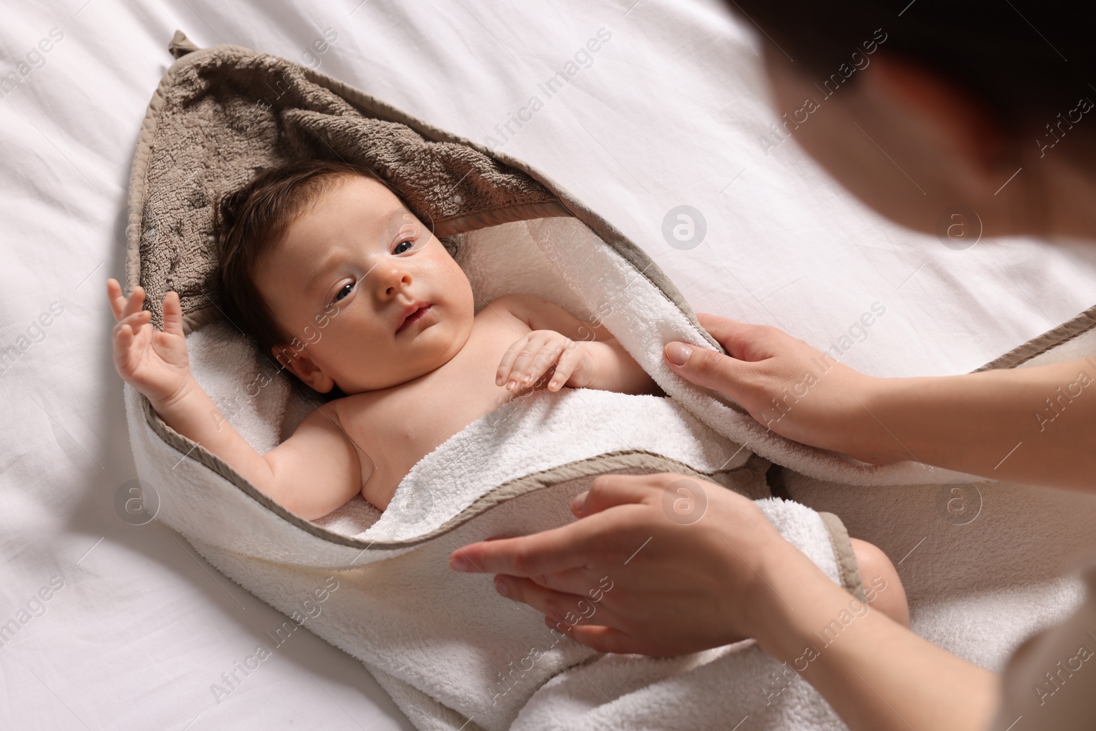 Photo of Mother wrapping her cute little baby with hooded towel after bathing on bed, above view