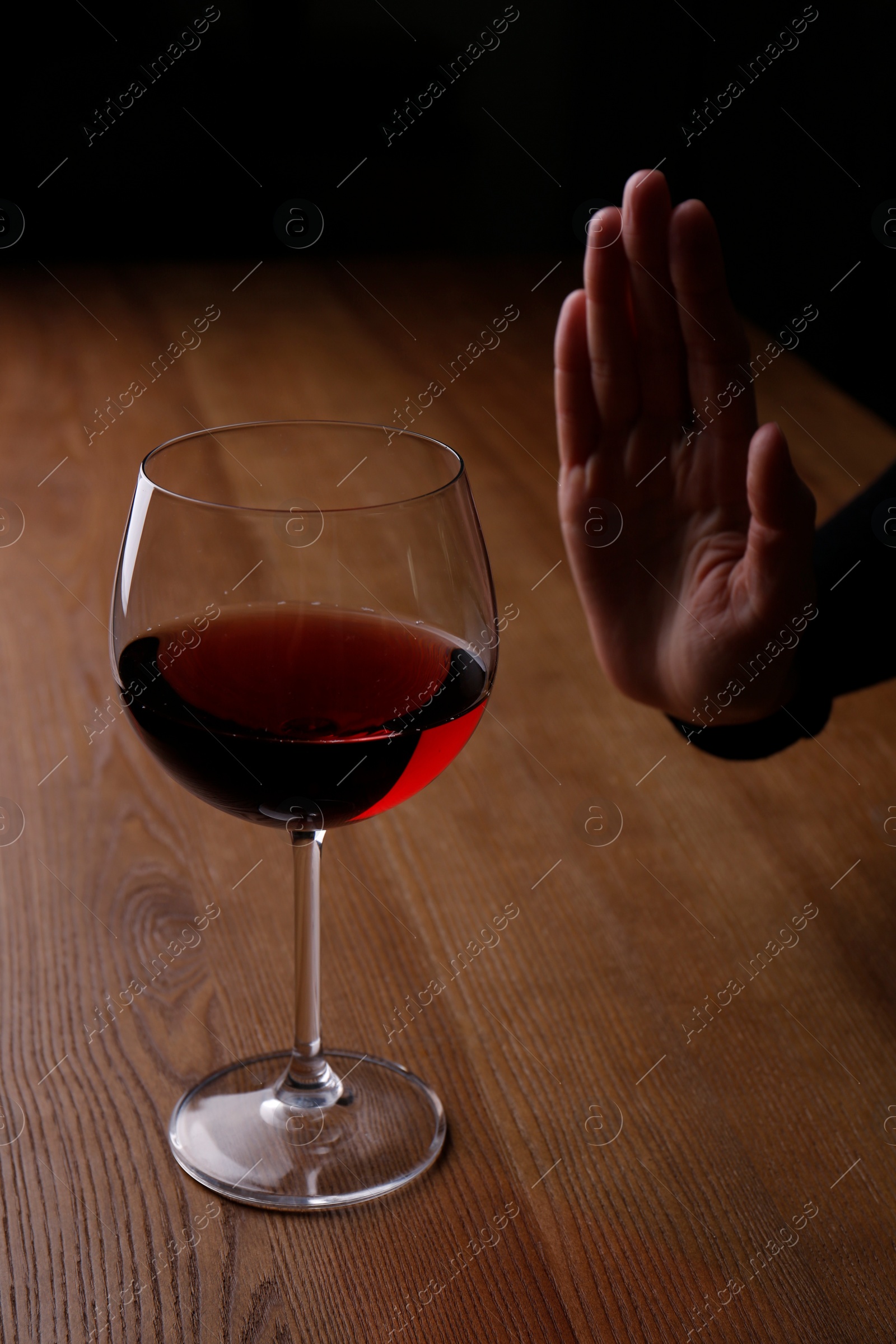 Photo of Man refusing to drink red wine at wooden table, closeup. Alcohol addiction treatment