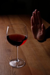 Photo of Man refusing to drink red wine at wooden table, closeup. Alcohol addiction treatment