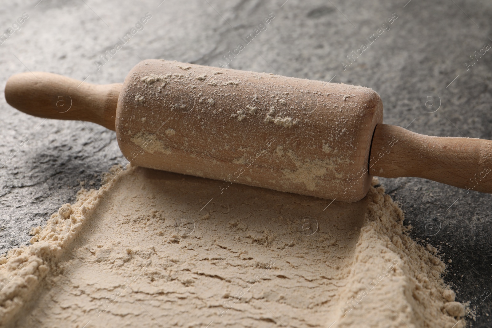 Photo of Scattered flour and rolling pin on grey textured table, closeup