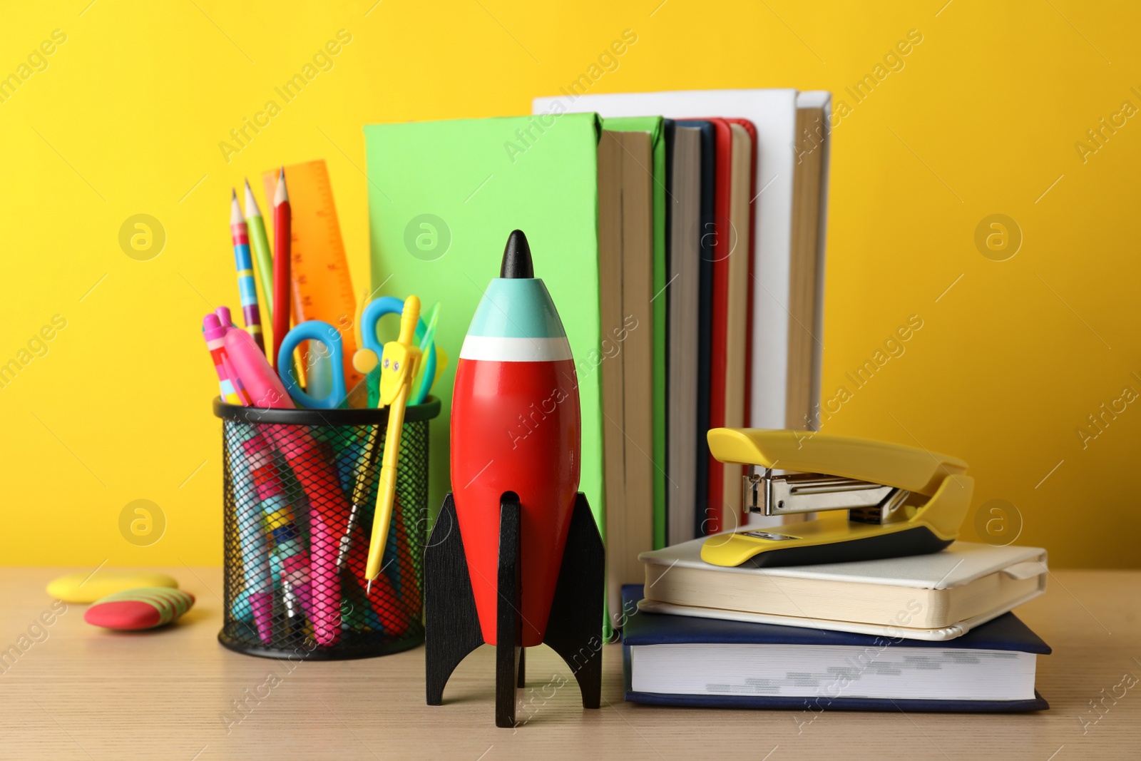 Photo of Bright toy rocket and school supplies on wooden table