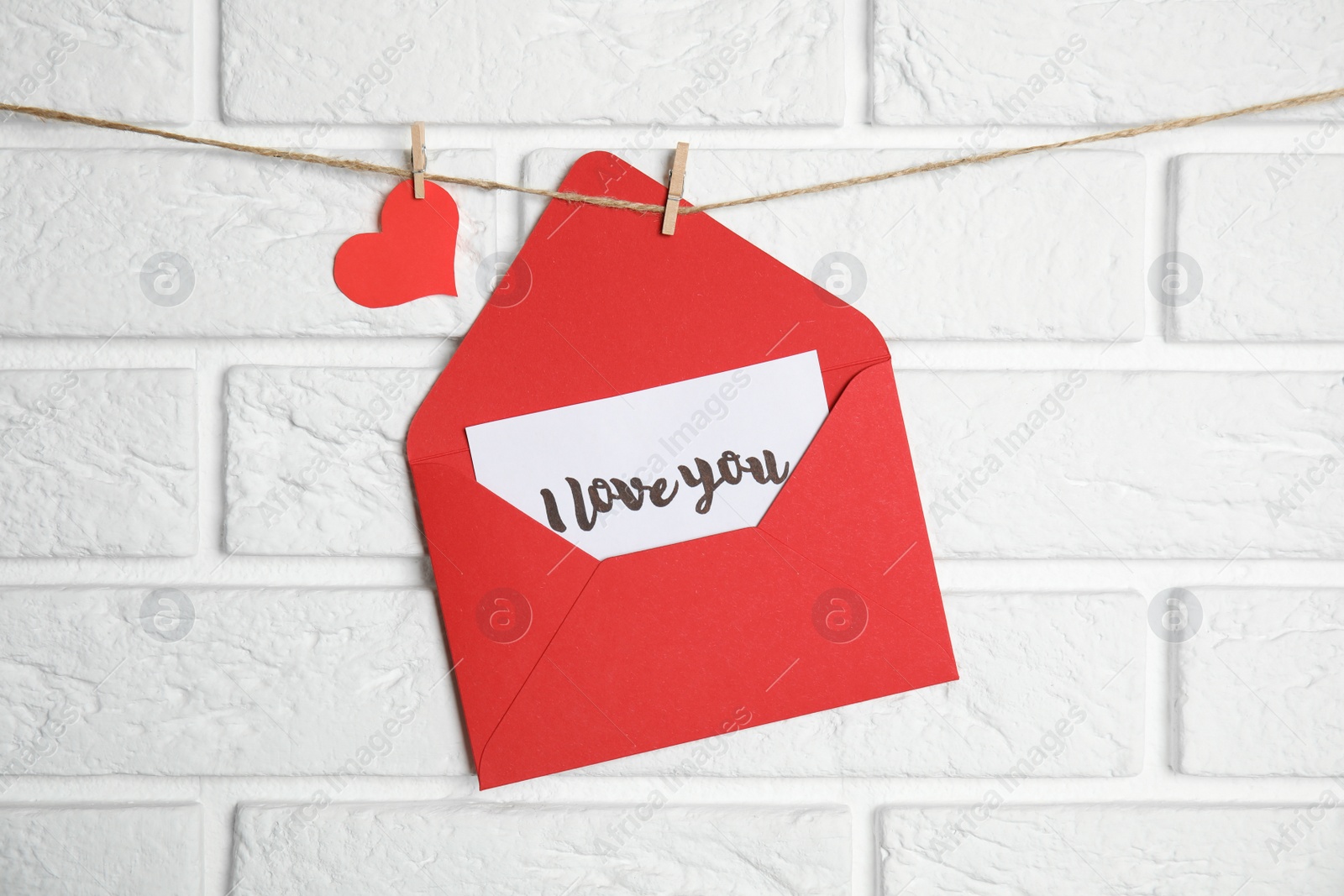 Photo of Envelope with I Love You card hanging on twine near white brick wall