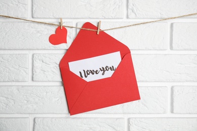 Envelope with I Love You card hanging on twine near white brick wall