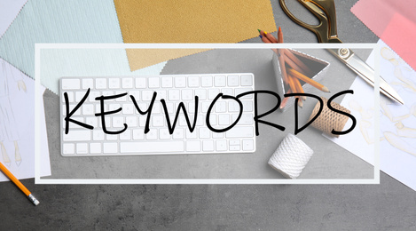 Image of Text KEYWORDS over designer's workplace with keyboard and accessories, flat lay