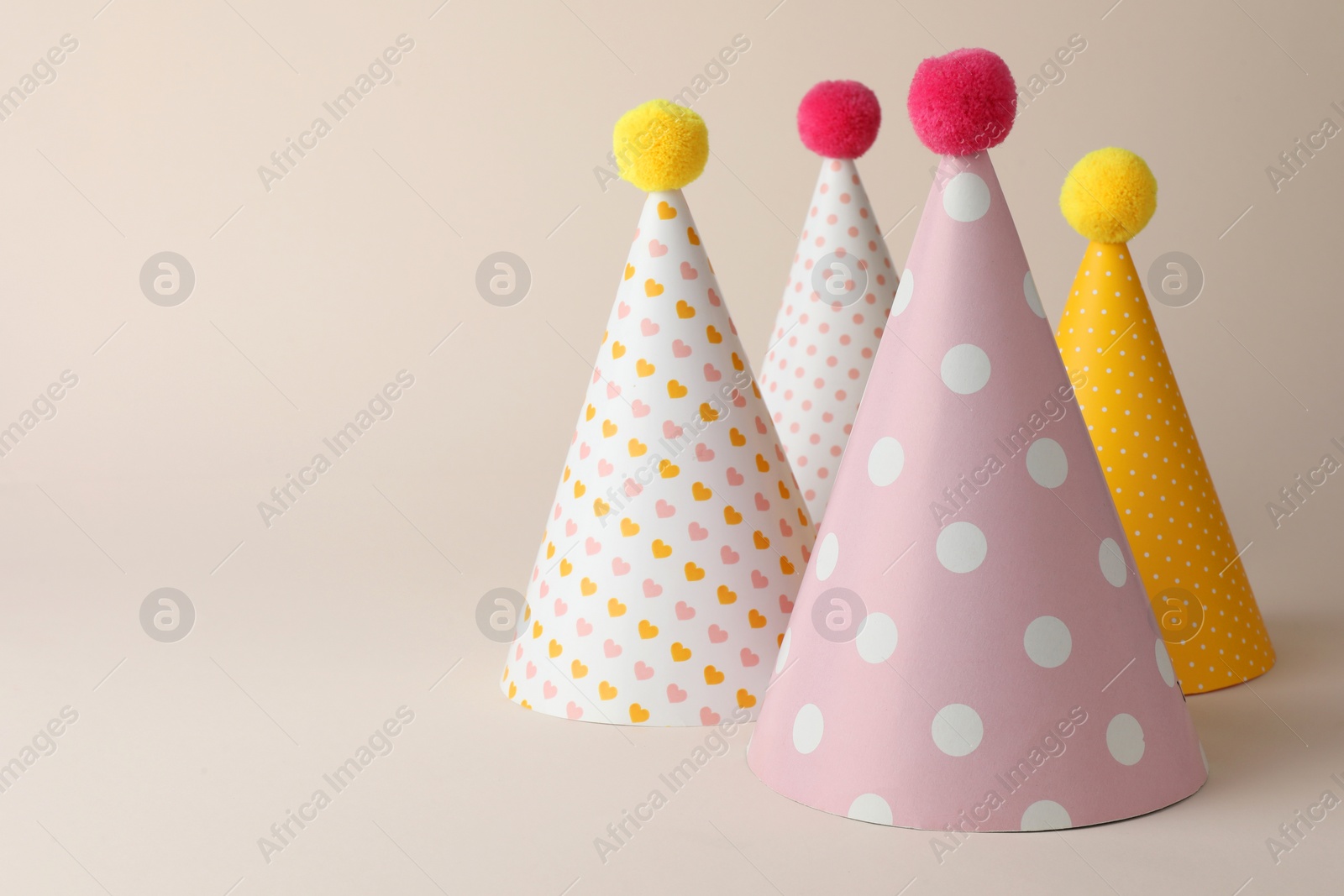 Photo of Beautiful party hats with pompoms on beige background. Space for text