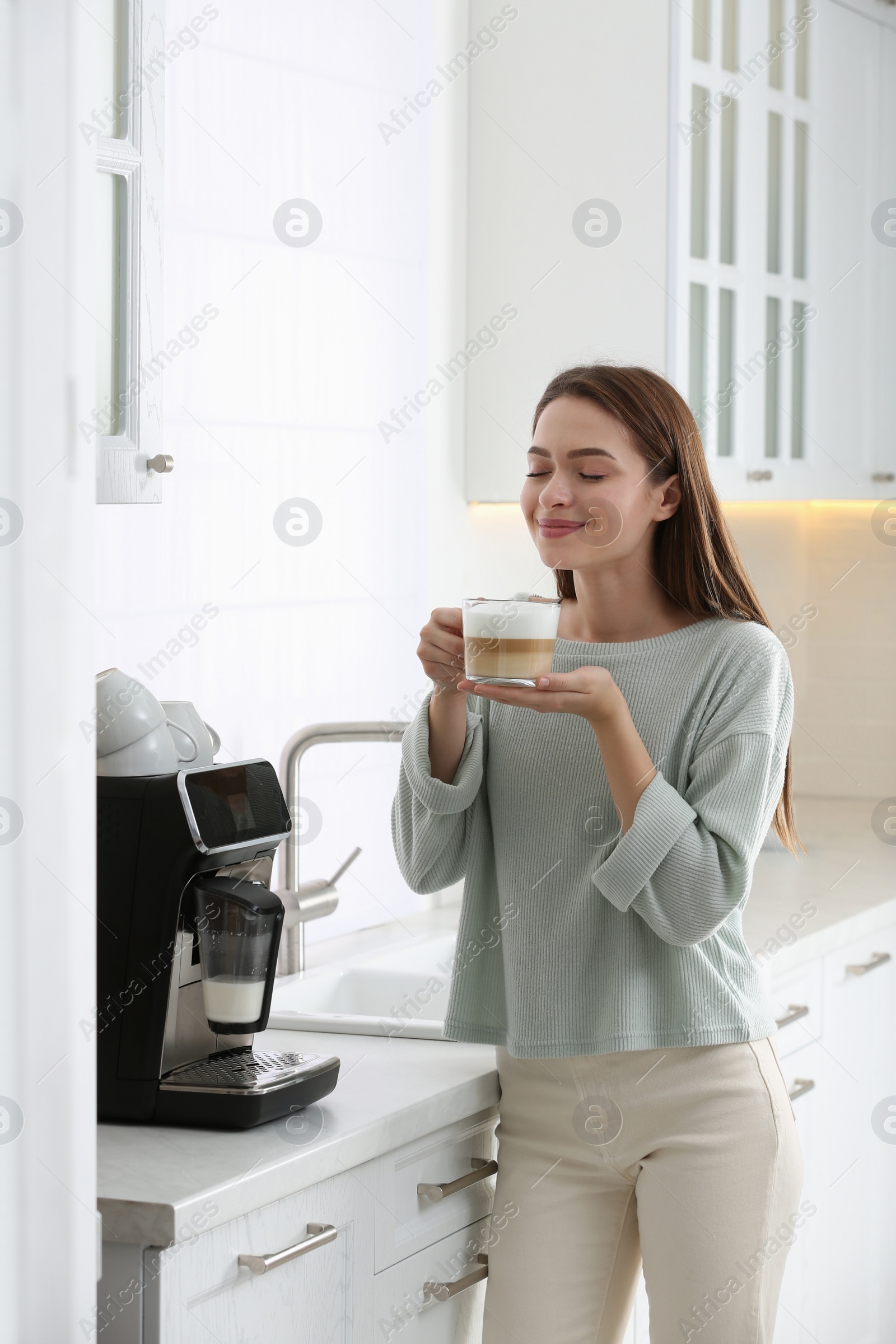 Photo of Young woman enjoying fresh aromatic coffee near modern machine in kitchen