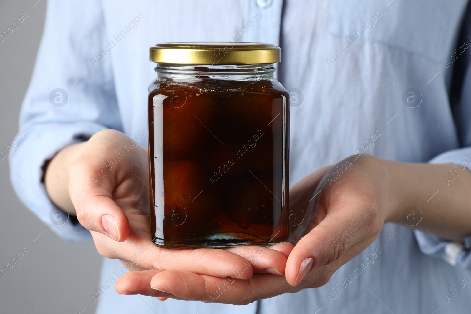 Photo of Woman holding jar of tasty sweet fig jam on grey background, closeup