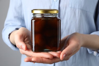 Woman holding jar of tasty sweet fig jam on grey background, closeup