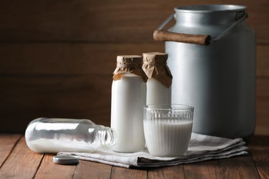 Photo of Tasty fresh milk in can, bottles and glass on wooden table, space for text