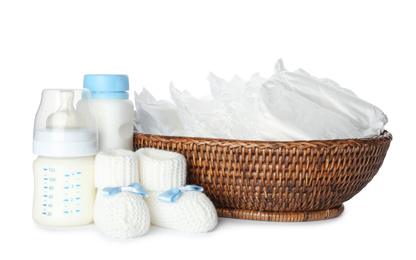Wicker bowl with disposable diapers, child's booties and bottles on white background