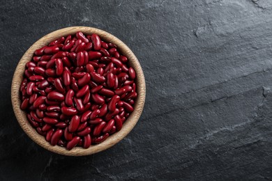 Photo of Raw red kidney beans in wooden bowl on black table, top view. Space for text