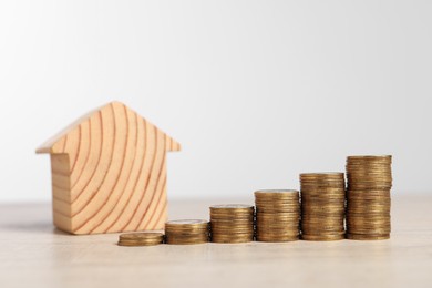Photo of Mortgage concept. House model and stacks of coins on wooden table against white background, space for text