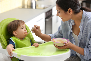 Young nanny feeding cute little baby in kitchen