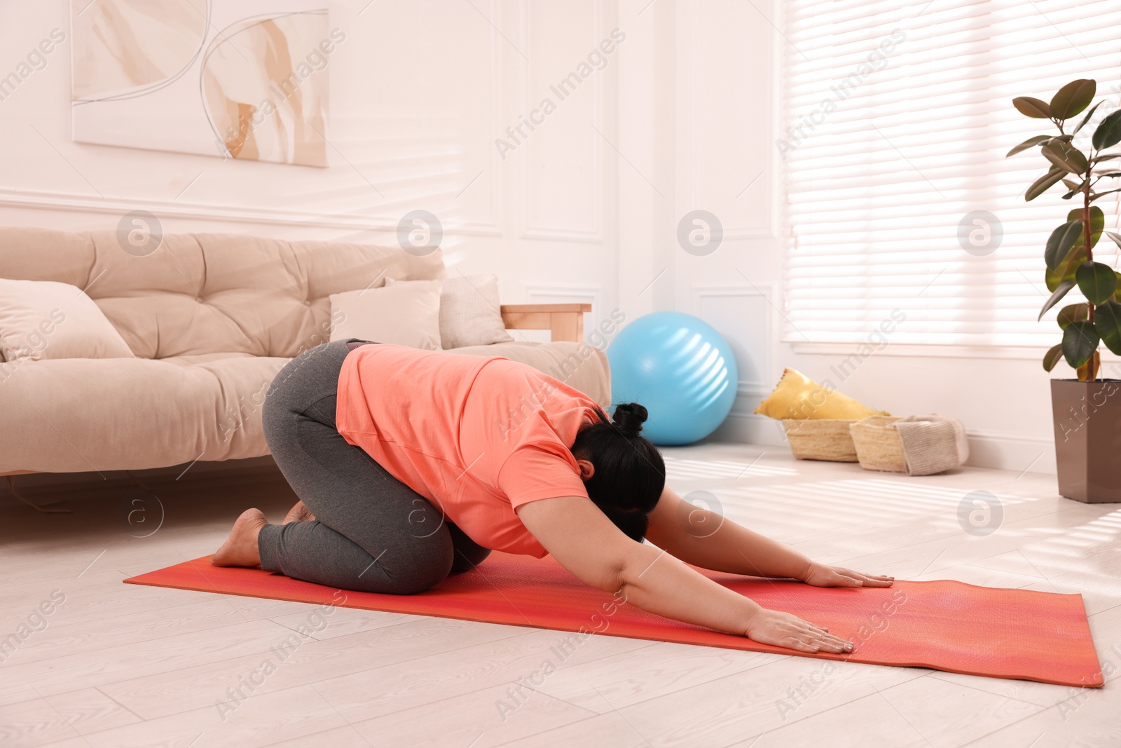 Photo of Overweight mature woman doing exercise on yoga mat at home