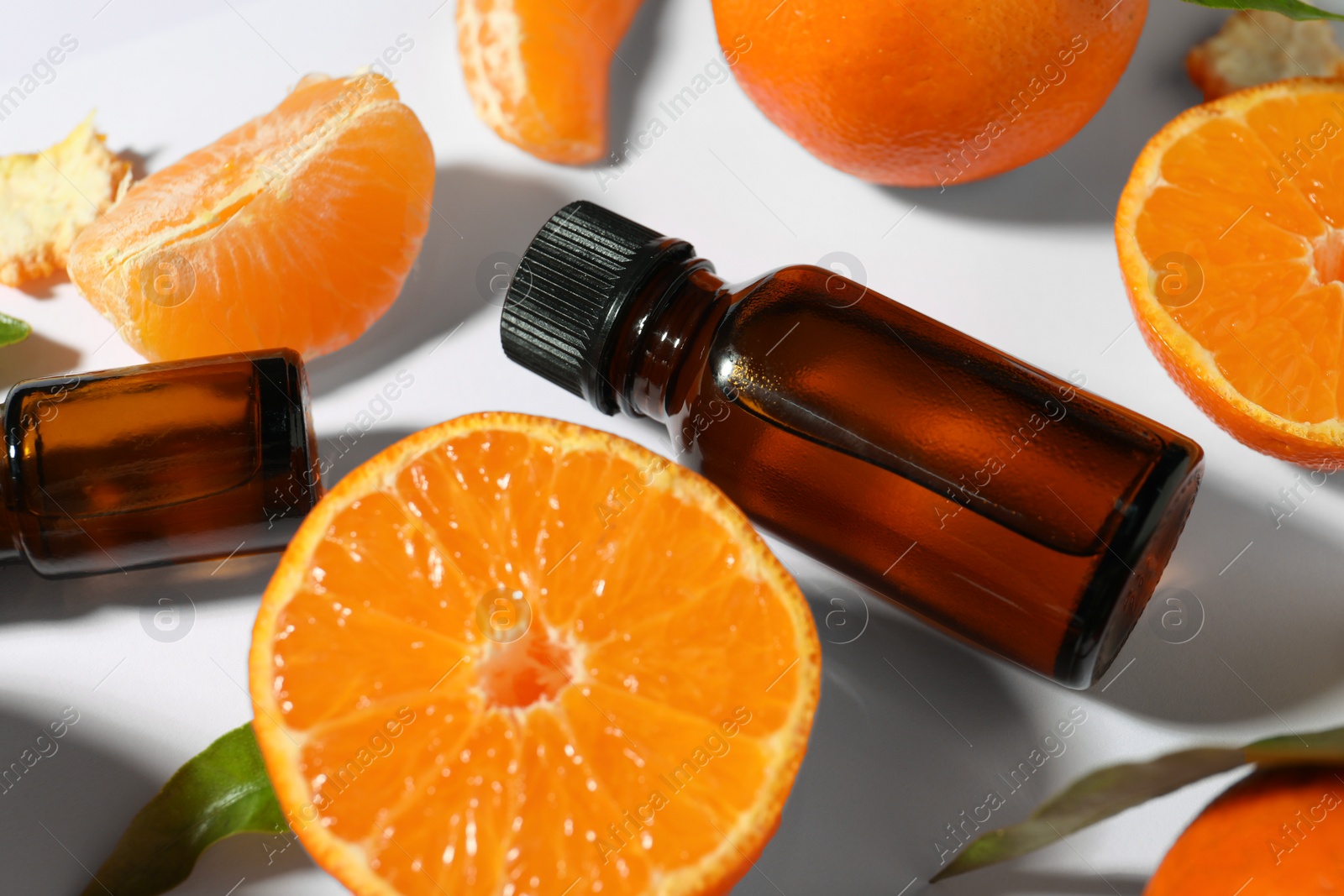 Photo of Aromatic tangerine essential oil in bottles and citrus fruits on white table, closeup