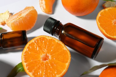 Photo of Aromatic tangerine essential oil in bottles and citrus fruits on white table, closeup