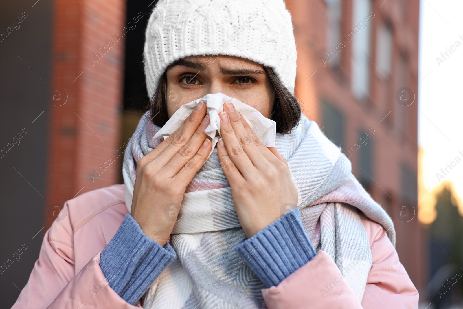 Photo of Woman with tissue blowing runny nose outdoors. Cold symptom