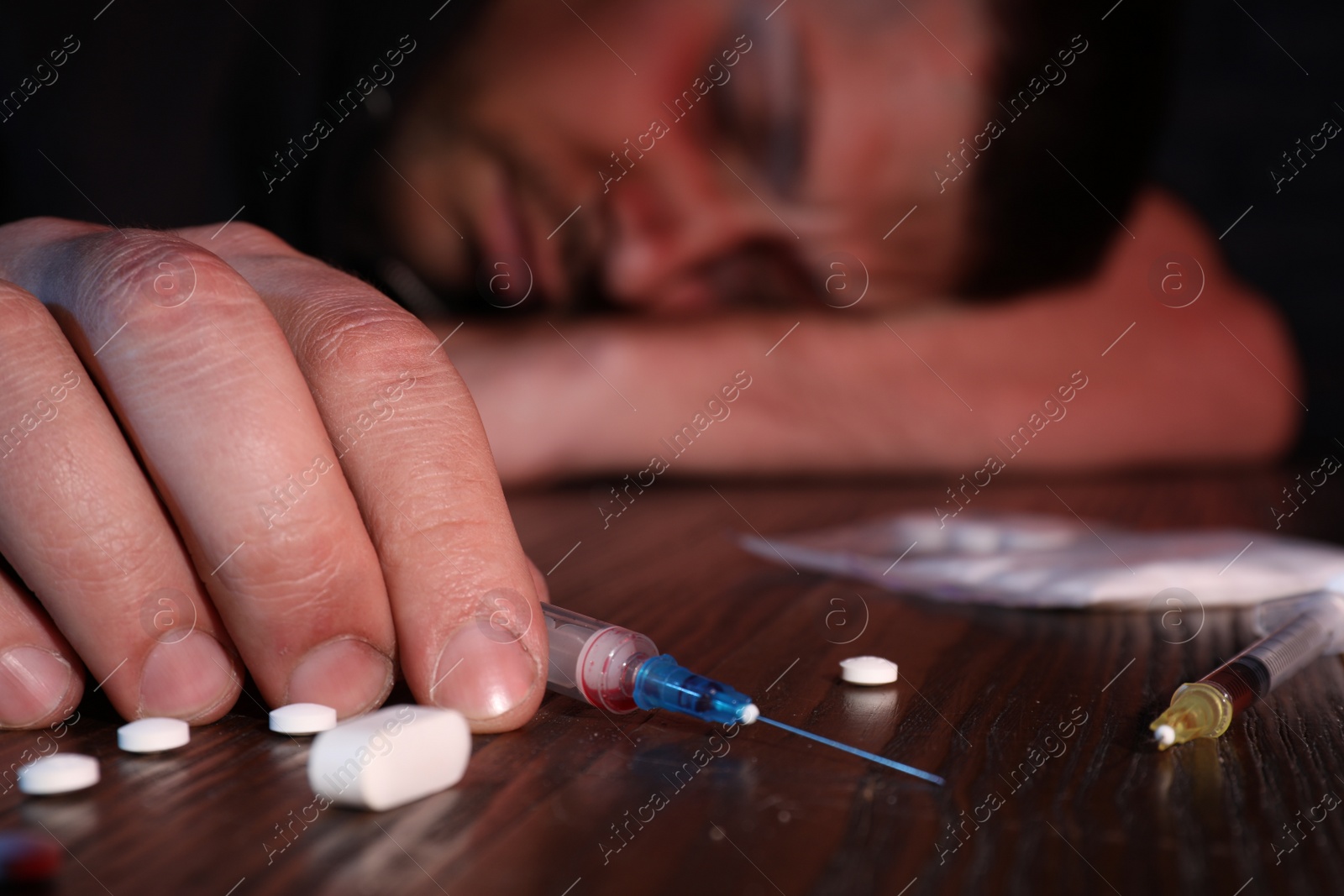 Photo of Overdosed man at table, focus on different drugs