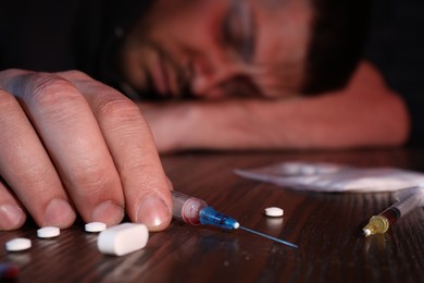 Photo of Overdosed man at table, focus on different drugs