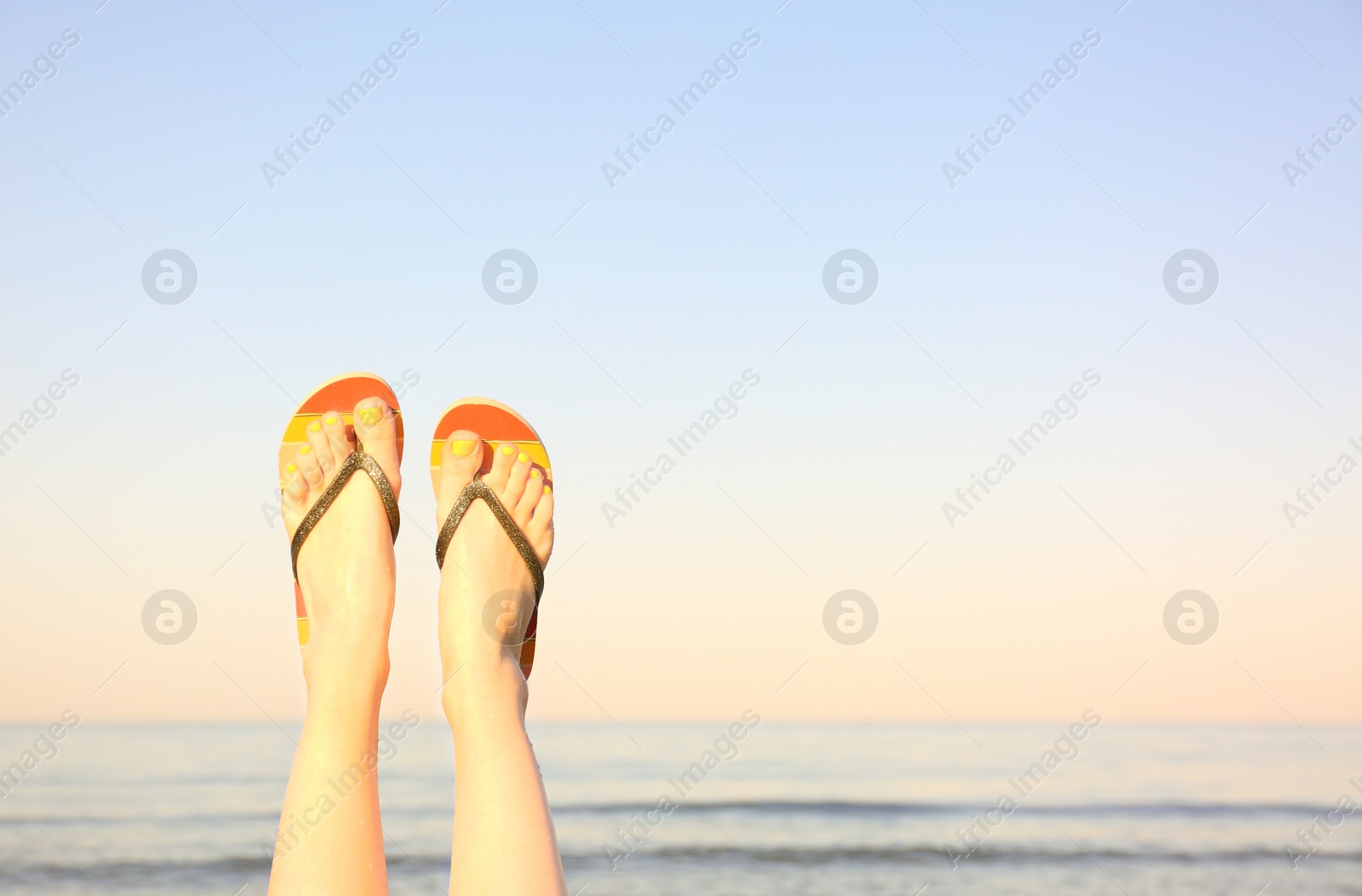 Photo of Closeup of woman wearing flip flops near sea, space for text. Beach accessories