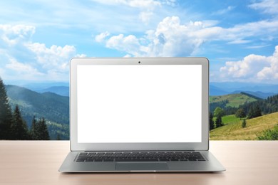 Image of Modern laptop with blank screen on table and view of beautiful mountain landscape