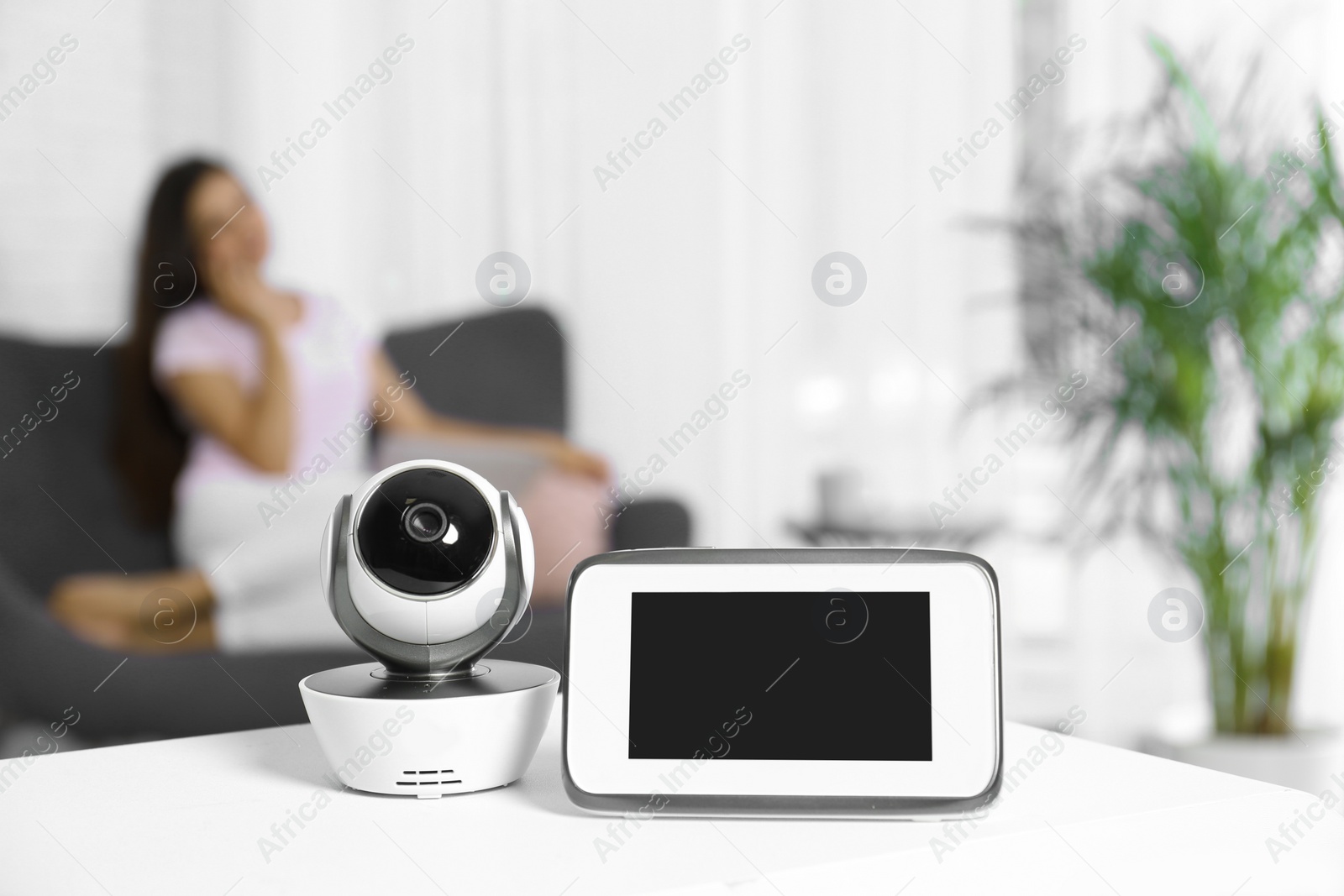 Photo of Baby monitor and camera on table and woman resting in living room. Video nanny