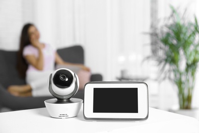 Photo of Baby monitor and camera on table and woman resting in living room. Video nanny