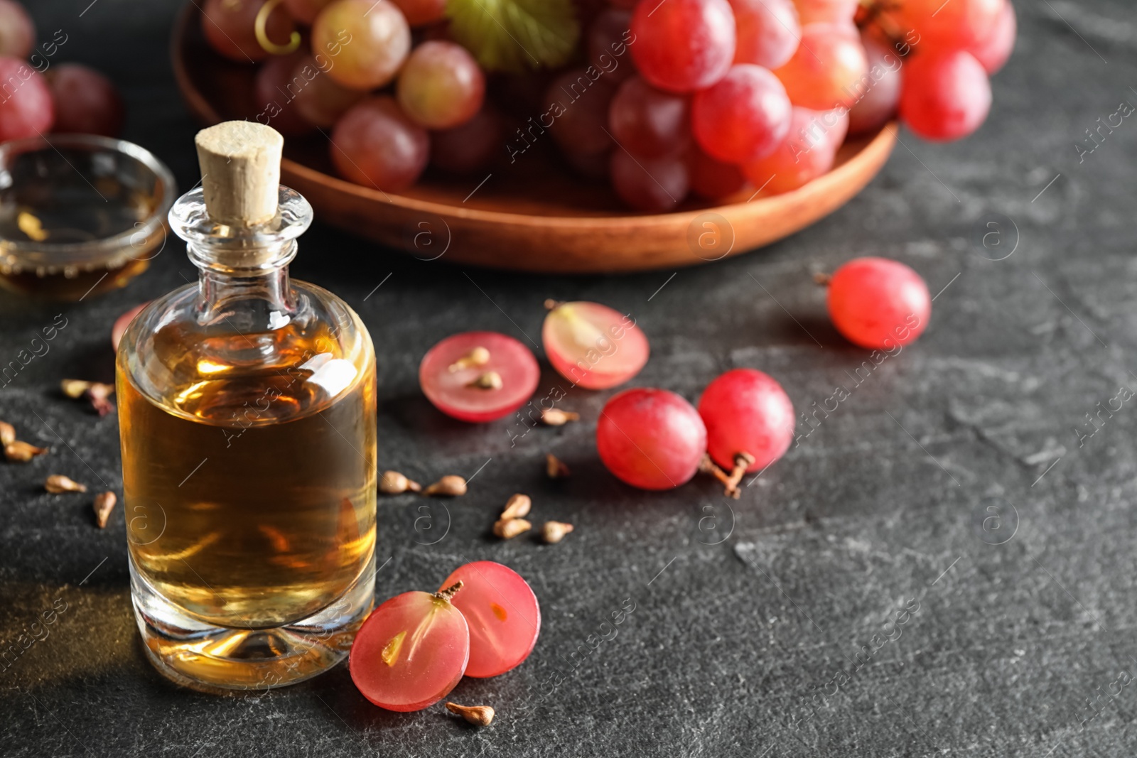 Photo of Organic red grapes, seeds and bottle of natural essential oil on black table. Space for text.