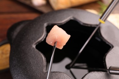 Fork with piece of raw meat over fondue pot, closeup
