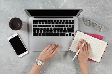 Photo of Woman working with modern laptop at marble table, top view