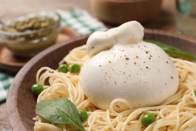 Bowl of delicious pasta with burrata, peas and spinach on table, closeup
