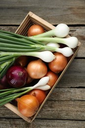 Crate with different kinds of onions on wooden table, top view