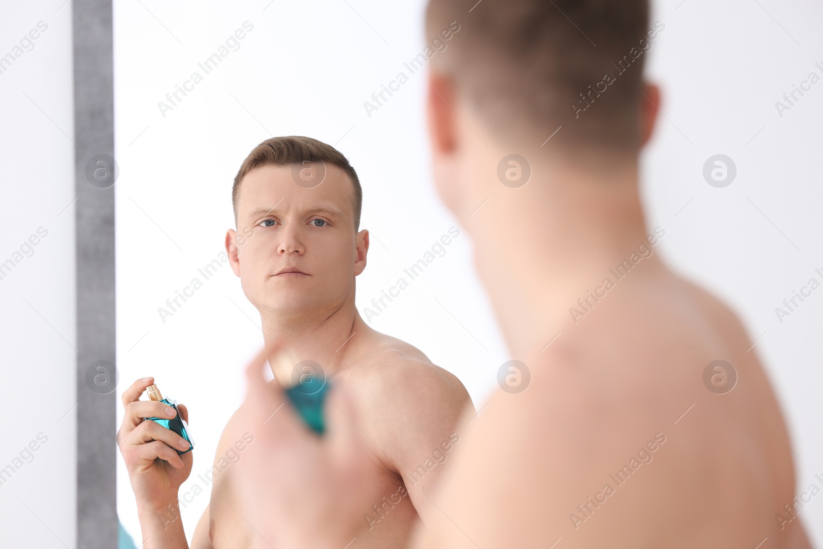 Photo of Handsome man using perfume in front of mirror