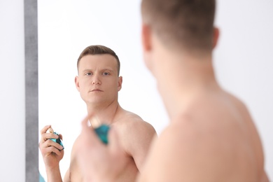 Photo of Handsome man using perfume in front of mirror