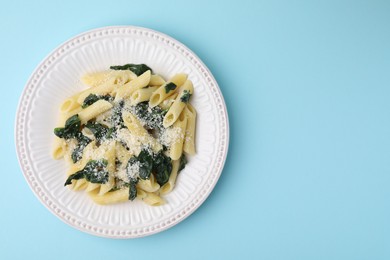 Photo of Tasty pasta with spinach and cheese on light blue table, top view. Space for text