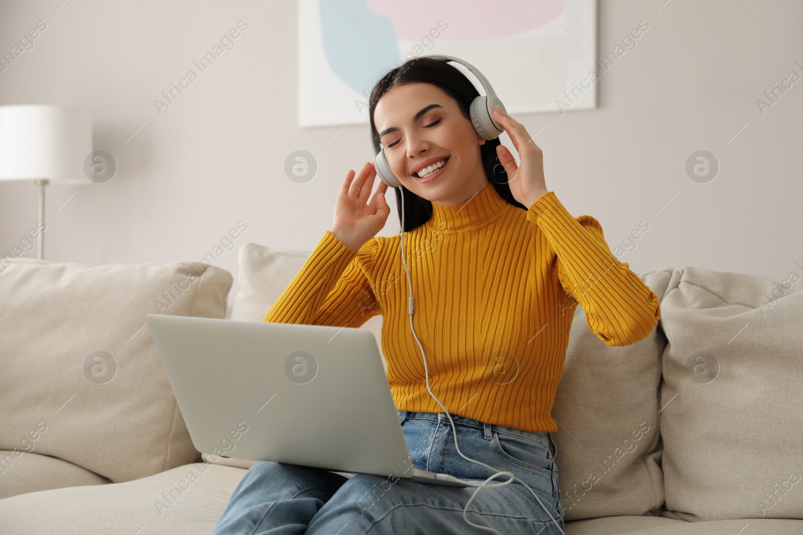 Photo of Woman with laptop and headphones sitting on sofa at home