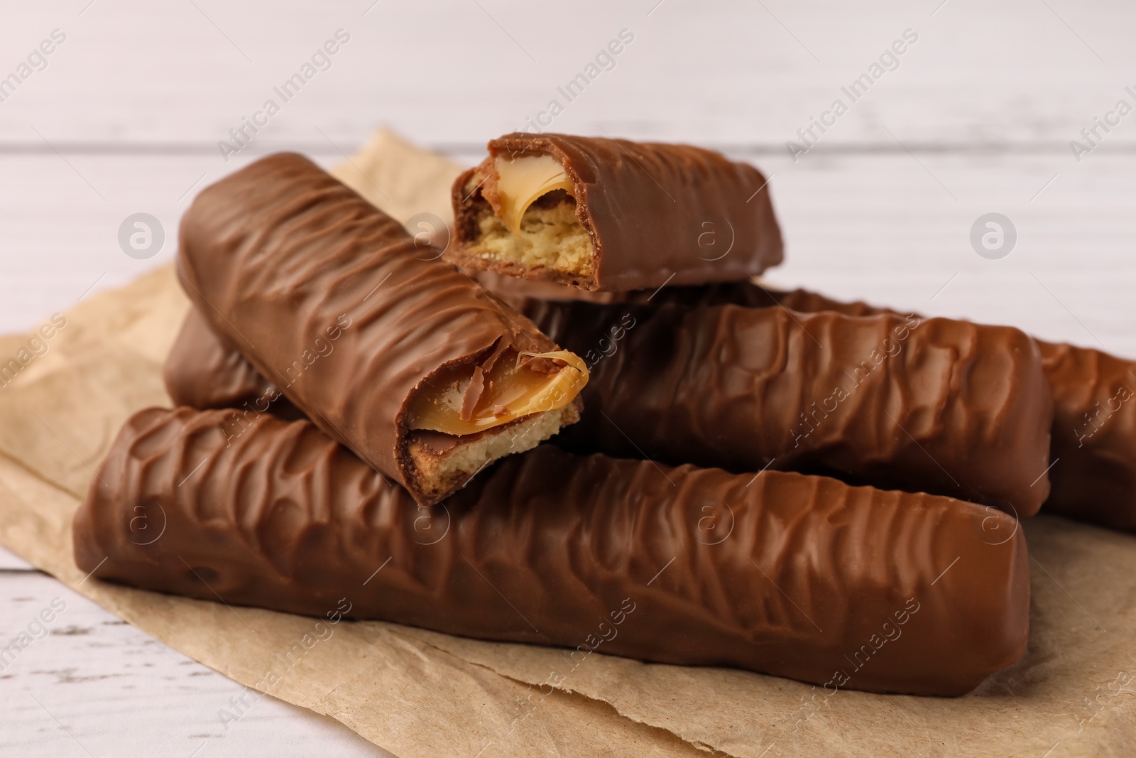 Photo of Tasty chocolate bars with caramel on white wooden table, closeup