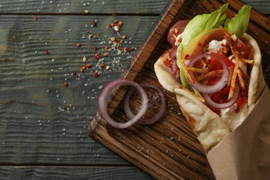 Delicious pita wrap with vegetables and meat on dark wooden table, top view. Space for text