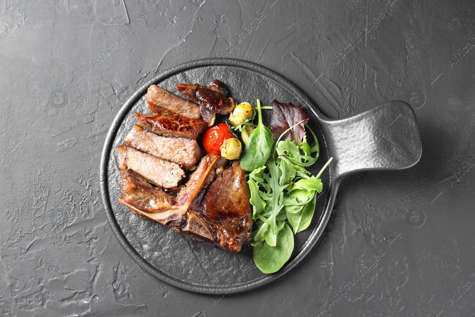 Photo of Delicious grilled beef meat, vegetables and greens on black table, top view