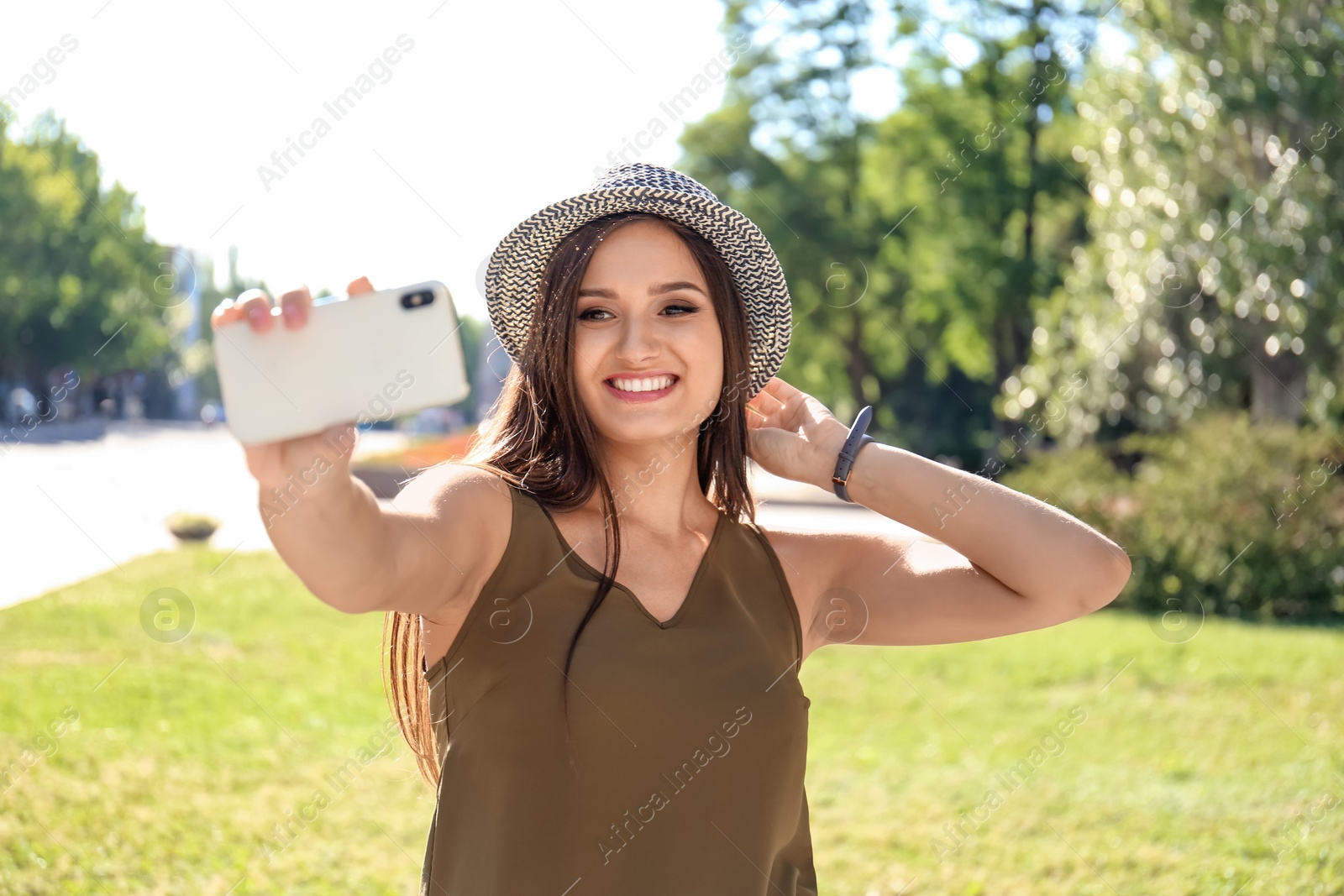 Photo of Young woman taking selfie outdoors on sunny day