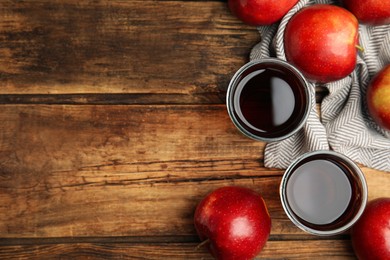 Delicious cider and ripe red apples on wooden table, flat lay. Space for text
