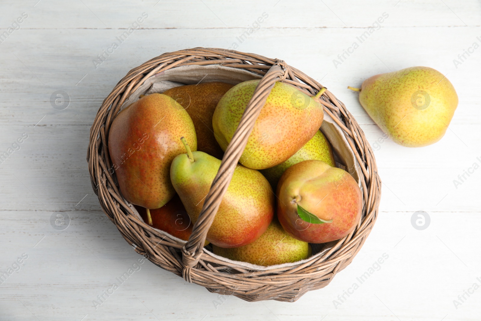 Photo of Ripe juicy pears in wicker basket on white wooden table, above view