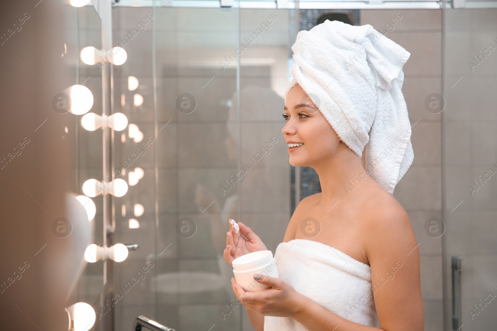 Photo of Beautiful woman with clean towels applying face cream in bathroom